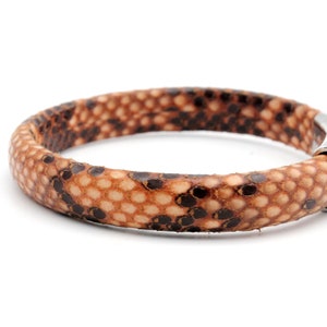 May include: A brown leather bracelet with a snakeskin pattern. The bracelet has a silver clasp.