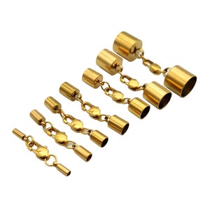 May include: A set of six gold-toned metal jewellery cord end caps with attached lobster claw clasps, arranged in a diagonal line from smallest to largest. Each piece features a cylindrical cap connected to a central lobster clasp by jump rings.