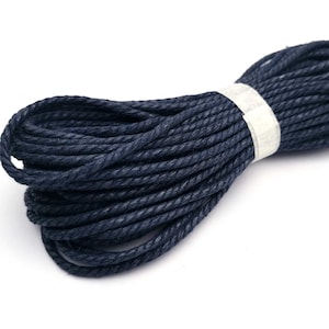 May include: A close-up of a spool of dark blue cotton cord. The cord is tightly wound and has a slightly textured surface.