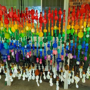 May include: A rainbow-colored wall hanging made from plastic bottle caps. The caps are strung together in rows, creating a colorful and whimsical design.