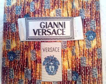 May include: A brown and yellow patterned silk tie with a white label that reads "Gianni Versace" and a smaller white label that reads "Versace".