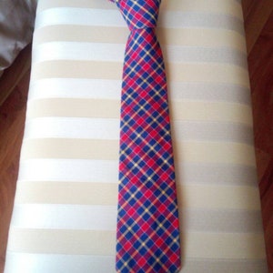 May include: A red, blue, and yellow plaid tie. The tie is made of a woven fabric and has a pointed tip.