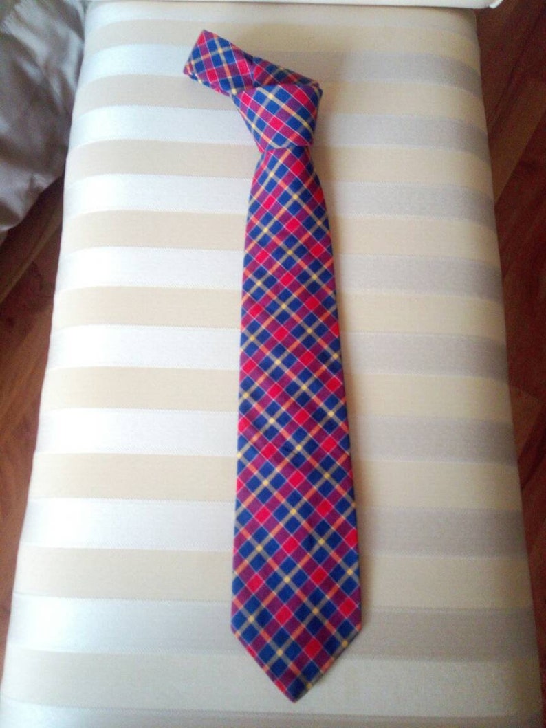 May include: A red, blue, and yellow plaid tie. The tie is made of a woven fabric and has a pointed tip.
