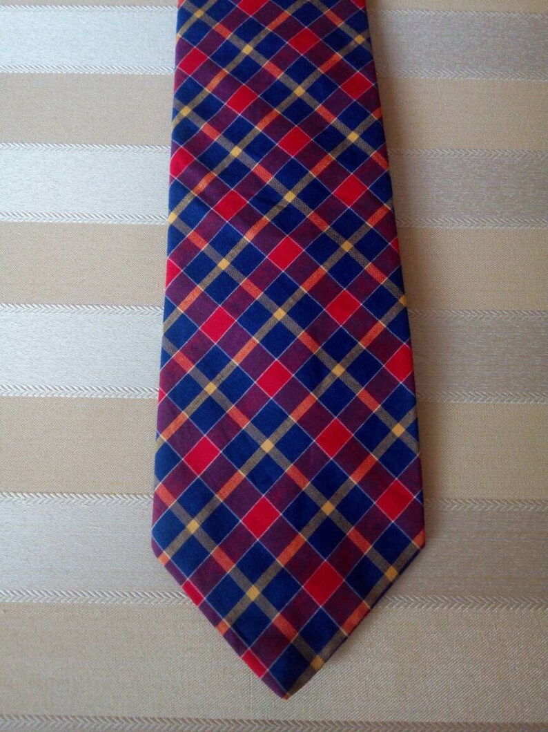 May include: A navy blue tie with a red, yellow, and burgundy plaid pattern.
