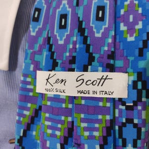May include: A blue, green, purple, and black patterned silk tie with a white label that reads "Ken Scott 100% Silk Made in Italy."