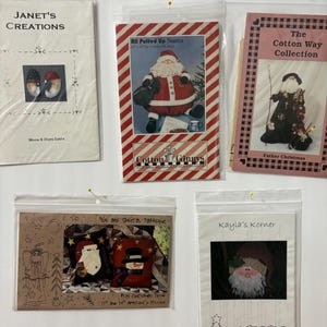 May include: A collection of Christmas-themed craft patterns in plastic sleeves, including designs for Santa Claus, snowmen, and angels. The patterns feature text such as "Janet's Creations" and "Kayla's Korner."