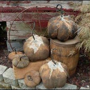 Op de afbeelding: Een verzameling van zes rustieke, handgemaakte stoffen pompoenen in verschillende maten. De pompoenen zijn gemaakt van jute en hebben een verweerde, vintage uitstraling. Ze worden tentoongesteld op een houten vat en een stenen muur.
