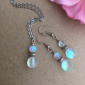 May include: A silver chain necklace and matching earrings with iridescent white glass beads. The beads have a silver accent.