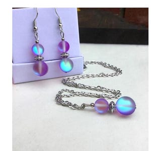 May include: A silver chain necklace with a iridescent purple and blue glass bead pendant. Matching iridescent purple and blue glass bead earrings with silver hooks are also included.