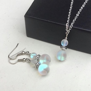 May include: A set of iridescent white opal jewelry with a silver chain necklace and matching earrings. The necklace and earrings feature a round opal bead with a silver accent.