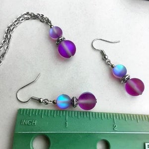 May include: A set of iridescent purple and blue glass bead earrings and a matching necklace. The beads are round and have a frosted finish. The jewelry is silver-toned.