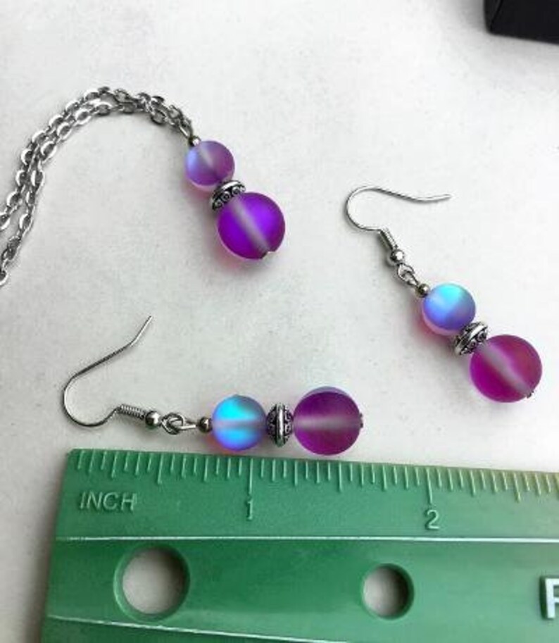 May include: A set of iridescent purple and blue glass bead earrings and a matching necklace. The beads are round and have a frosted finish. The jewelry is silver-toned.