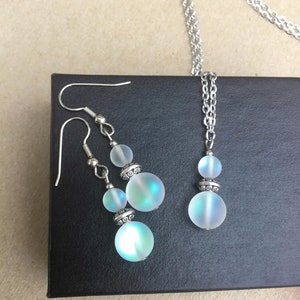 May include: A silver chain necklace and matching earrings with iridescent white glass beads. The beads have a silver trim.