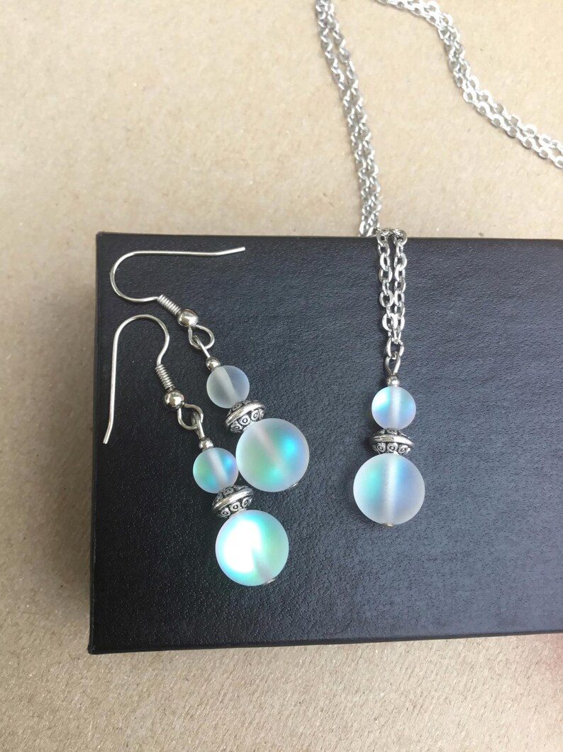 May include: A silver chain necklace and matching earrings with iridescent white glass beads. The beads have a silver trim.