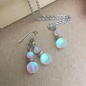 May include: A silver chain necklace and earrings with iridescent white glass beads. The beads have a silver metal accent.