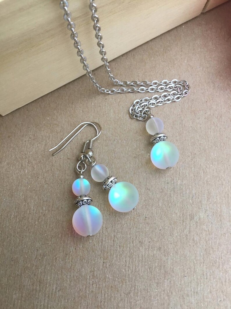 May include: A silver chain necklace and earrings with iridescent white glass beads. The beads have a silver metal accent.