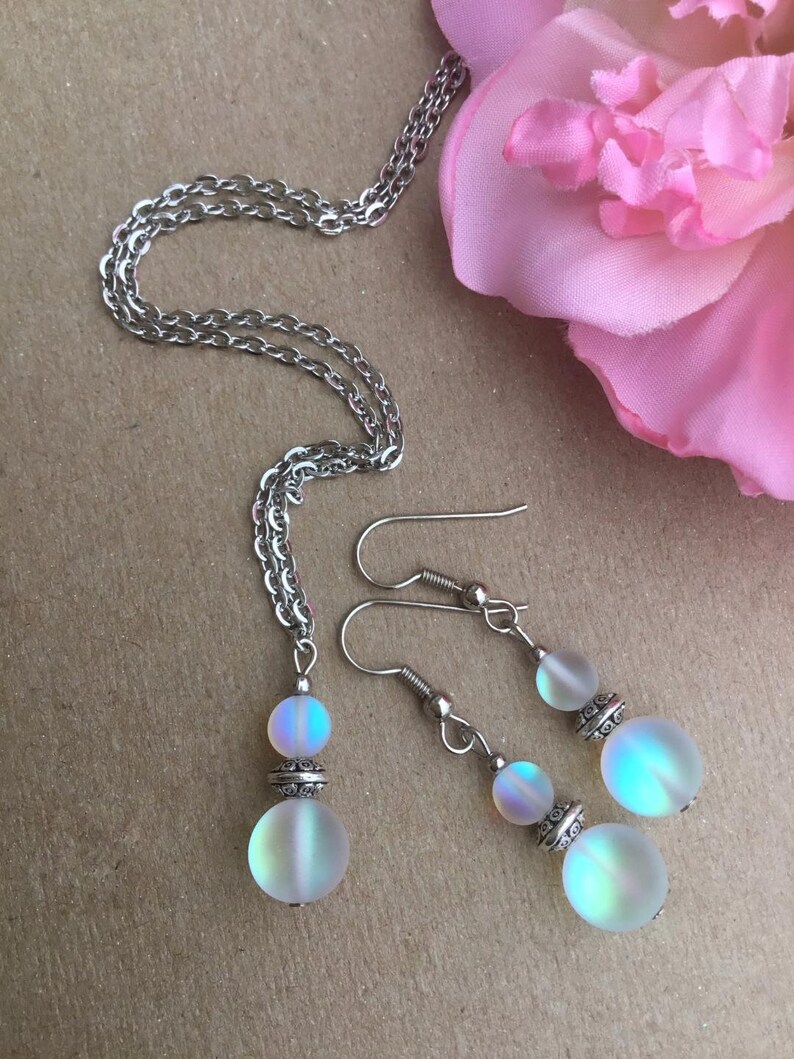 May include: A silver chain necklace and matching earrings with iridescent white glass beads. The beads have a silver accent.