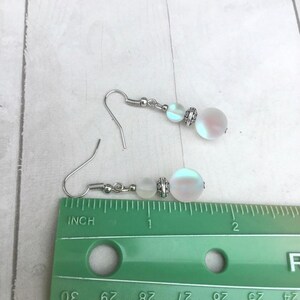 May include: A pair of silver earrings with iridescent white beads. The beads are approximately 1/2 inch in diameter. The earrings are measured against a ruler.
