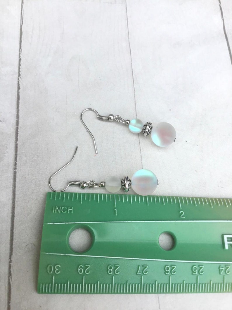 May include: A pair of silver earrings with iridescent white beads. The beads are approximately 1/2 inch in diameter. The earrings are measured against a ruler.