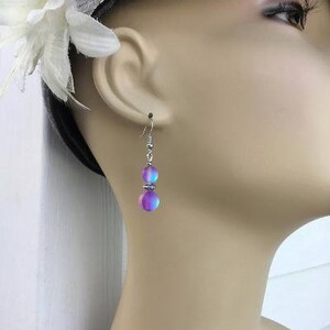 May include: A pair of silver earrings with iridescent purple and blue beads. The beads are round and have a smooth, polished finish.