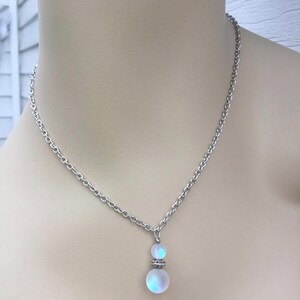 May include: A silver chain necklace with a iridescent white glass pendant. The pendant is made of two round beads, one larger than the other.