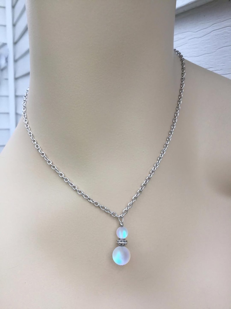 May include: A silver chain necklace with a iridescent white glass pendant. The pendant is made of two round beads, one larger than the other.
