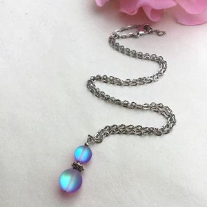 May include: A silver chain necklace with a iridescent blue and purple pendant featuring two round beads.