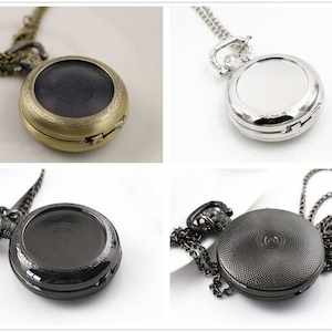 Peut inclure: Quatre montres de poche avec chaînes, chacune avec une finition différente : or antique, argent, noir et noir texturé. Les montres sont toutes rondes et ont un design classique.