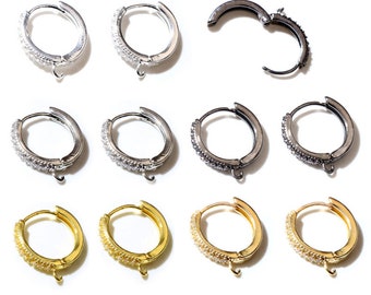May include: A selection of hoop earrings in silver, black, and gold. Some are open, revealing a hinged design. The earrings are embellished with tiny, sparkling stones, and each has a small loop for attaching charms or other adornments.