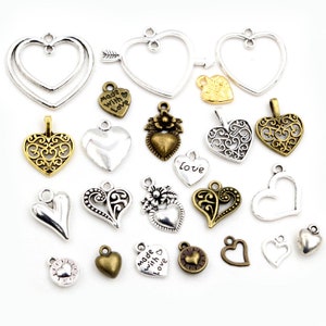 K&ouml;nnte beinhalten: Sortiment an silbernen und bronzenen herzf&ouml;rmigen Charms mit verschiedenen Designs, darunter Filigran, Blumen und einfache Herzformen. Einige Charms haben die Aufschrift "Made with Love" und "Love".