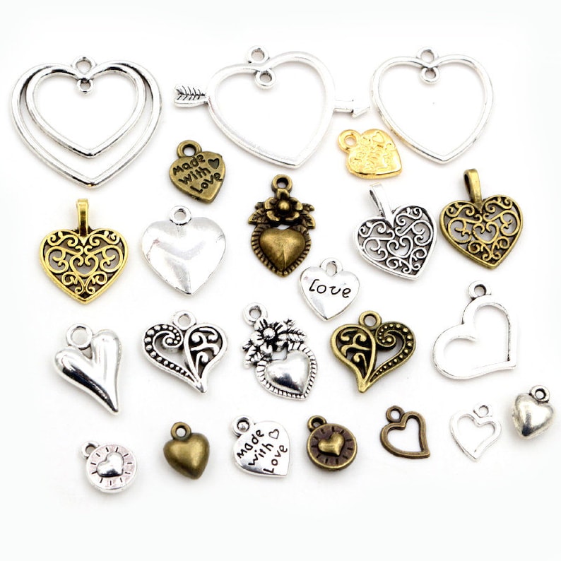 K&ouml;nnte beinhalten: Sortiment an silbernen und bronzenen herzf&ouml;rmigen Charms mit verschiedenen Designs, darunter Filigran, Blumen und einfache Herzformen. Einige Charms haben die Aufschrift "Made with Love" und "Love".