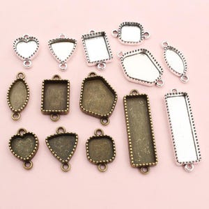 Puede incluir: Una colección de colgantes de bisel metálicos en varias formas, incluyendo corazones, triángulos, cuadrados y óvalos. Los colgantes tienen un acabado plateado o bronce y están diseñados para la fabricación de joyas. Cada colgante tiene un lazo.