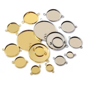 Puede incluir: Una colección de bandejas colgantes de metal dorado y plateado de varios tamaños. Cada bandeja tiene una base circular y pequeños bucles para sujetar cadenas u otros componentes. Las bandejas están dispuestas sobre una superficie blanca.