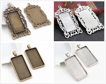 May include: A collection of rectangular pendant trays in various metallic finishes. The trays feature ornate filigree frames and simple bezel settings, perfect for jewelry making. The colors include antique bronze, silver, and gold tones.