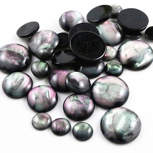 Peut inclure: Assortiment de cabochons ronds irisés dans des tons de noir, gris et rose. Les cabochons sont lisses et ont une finition nacrée.
