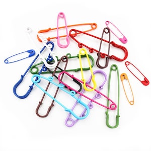 Può includere: Una collezione di spille di sicurezza colorate di diverse dimensioni. Le spille sono in metallo e hanno una finitura lucida. Sono disposte in modo casuale su uno sfondo bianco.