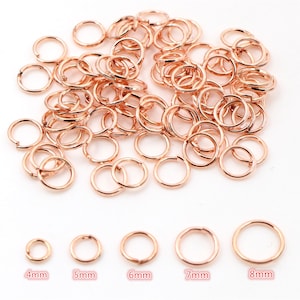 May include: A large pile of rose gold jump rings in various sizes. The rings are arranged in a pile on a white background. There are five individual rings below the pile, labelled 4mm, 5mm, 6mm, 7mm, and 8mm.