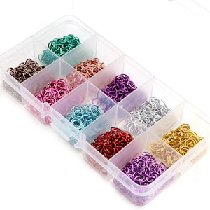 Könnte beinhalten: Eine transparente Plastik-Aufbewahrungsbox mit 10 Fächern, gefüllt mit bunten Metall-Sprühringen. Die Ringe sind in verschiedenen Farben, darunter Silber, Gold, Rot, Lila, Blau und Grün.