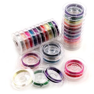 以下が含まれることがあります： 透明なプラスチック容器に入ったカラフルなワイヤーのスプールのアソートメント。スプールは積み重ねられ、白い表面に配置されています。