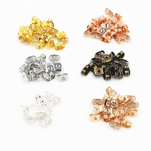 May include: Assortment of earring backs in four different colors: gold, rose gold, silver, and bronze. Each color is in a separate pile.
