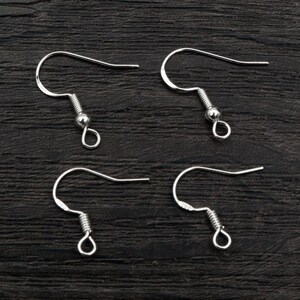 May include: Four silver earring hooks with a spring closure. The hooks are on a dark wood surface.