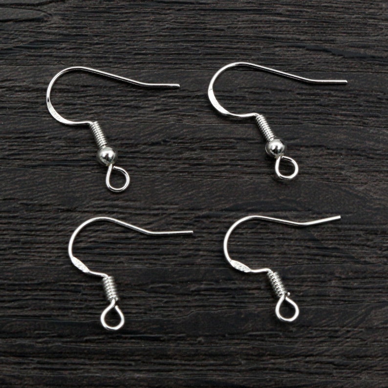 May include: Four silver earring hooks with a spring closure. The hooks are on a dark wood surface.