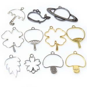 May include: Assortment of metal pendant blanks in various shapes, including a whale, umbrella, clover, fan, mushroom, leaf, and flower. The blanks are silver, gold, and black.