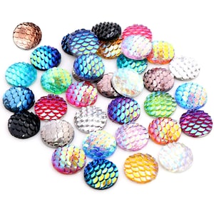 Puede incluir: Surtido de cabujones redondos iridiscentes con un patrón de escamas de sirena en varios colores, incluidos azul, verde, rosa, morado y dorado.