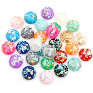 May include: Assortment of round, flat-backed cabochons with iridescent and gold flake accents. The cabochons are in various colours, including pink, blue, green, purple, orange, and white.