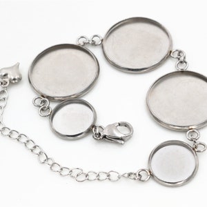 Könnte beinhalten: Ein silbernes Armband mit vier runden, leeren, silberfarbenen, glasartigen, gefassten Einstellungen. Das Armband hat eine silberne Kette und einen silbernen Verschluss.