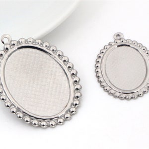 May include: Two silver oval pendant trays with a beaded border. The larger tray is approximately 5 cm in length and the smaller tray is approximately 4 cm in length.