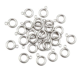 May include: A pile of silver jump rings with a soldered loop on each ring. The rings are scattered on a white background.