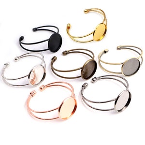 Può includere: Sei braccialetti rigidi in metallo di diversi colori con un cabochon rotondo di vetro al centro. I braccialetti sono disponibili in argento, oro, oro rosa e nero.