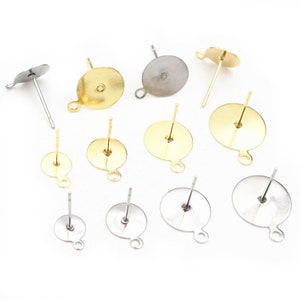 May include: An assortment of earring posts in gold and silver tones. The posts have a flat, round base with a loop and a straight post for insertion. The earring findings are arranged on a white surface.
